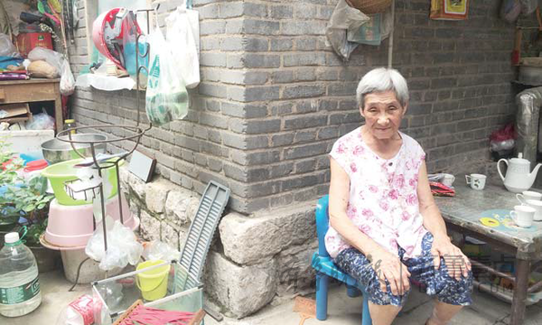 90岁高寿的张桂贞老人安详地坐在院子里。记者 许建立 摄 在济南泉城路北侧,有一条不起眼的小巷子,夹在皇亭体育馆和华能大厦之间,这里就是东箭道街。同金街的繁华相比,东箭道街显得破落。沿着巷子走进去,一片平房让时间仿佛凝固在上世纪60年代。传统的两扇式木制大门、低矮的平房、不规则的院落布局,狭窄的过道,潮湿的屋内环境,这里的居民怀着复杂的心态等待着老街巷的蝶变。 老人老屋老树 绘出老街的时光画卷 东箭道街得名,是因为这里在明清时期是驻军官兵骑马射箭之地。1949年前,东箭道街附近是济南城中最底层穷苦百姓